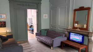 Una sala de estar con sofá, televisor, chimenea y puerta que da a otra habitación.