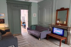 Ein Wohnzimmer mit einer Couch, einem Fernseher, einem Kamin und einer Tür zu einem anderen Raum.