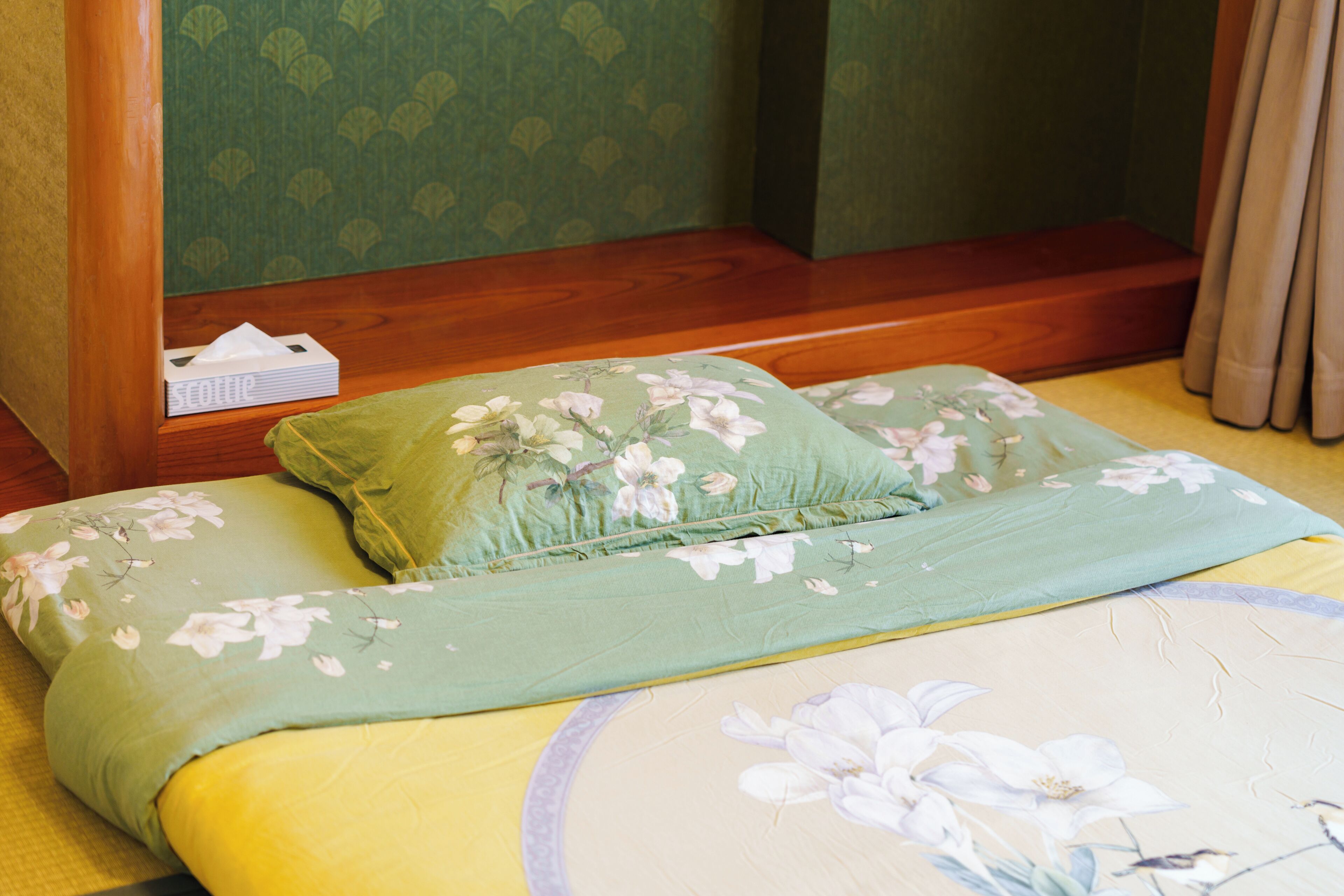 A room with a bed, a green floral bedspread, and a wooden headboard.