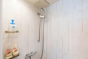 Un baño con ducha, un secador de manos y dos botellas de champú en un estante.