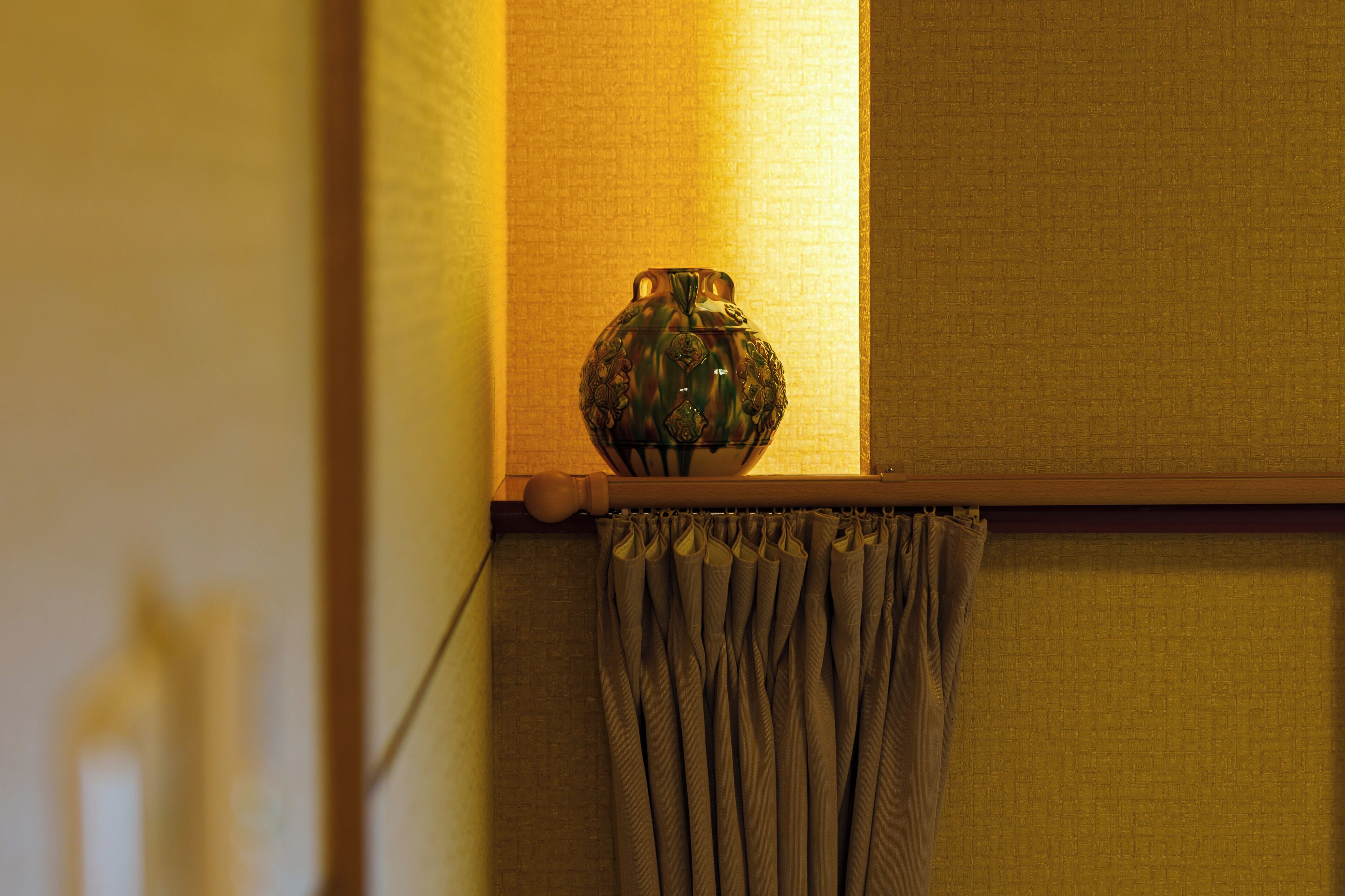 A vase on a shelf with a curtain below.