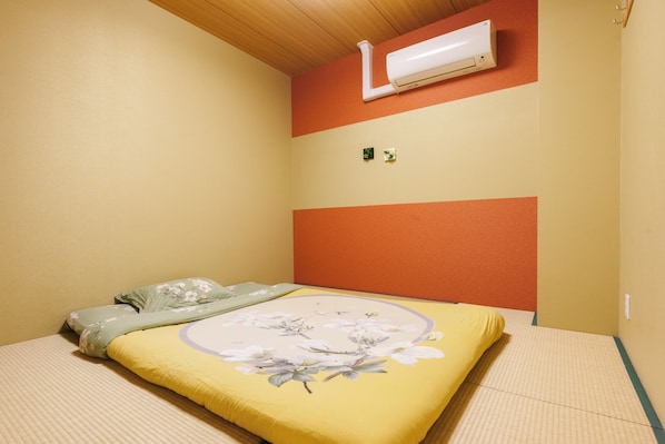 Un dormitorio con una cama, aire acondicionado instalado en la pared y una planta pequeña.