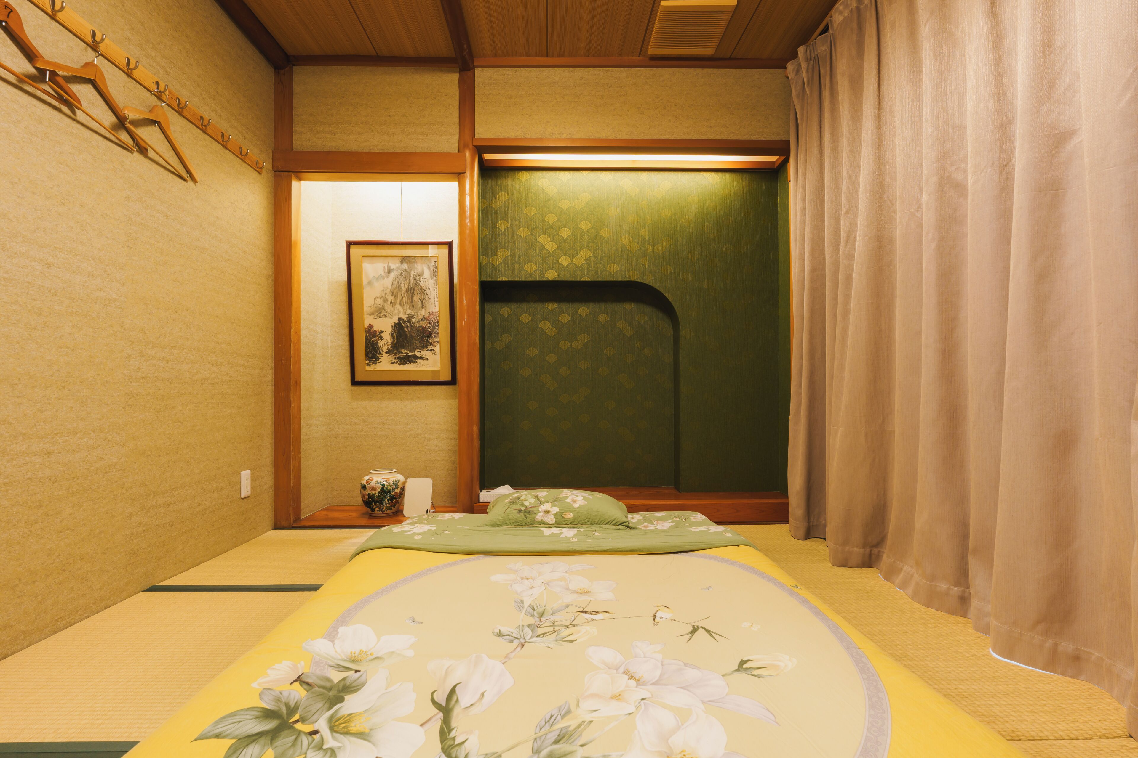 A traditional Japanese room with tatami flooring, a futon bed, a shoji screen, and a small table with a vase.