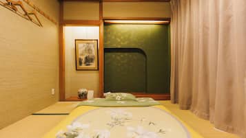 A traditional Japanese room with tatami flooring, a futon bed, a shoji screen, and a small table with a vase.