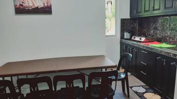 Une cuisine avec une table et des chaises, un tableau représentant des voiliers et une vue sur la verdure à l’extérieur.