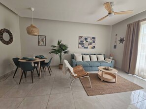Ein modernes Wohnzimmer mit Essbereich, Deckenventilator, großer Pflanze und blauem Sofa.