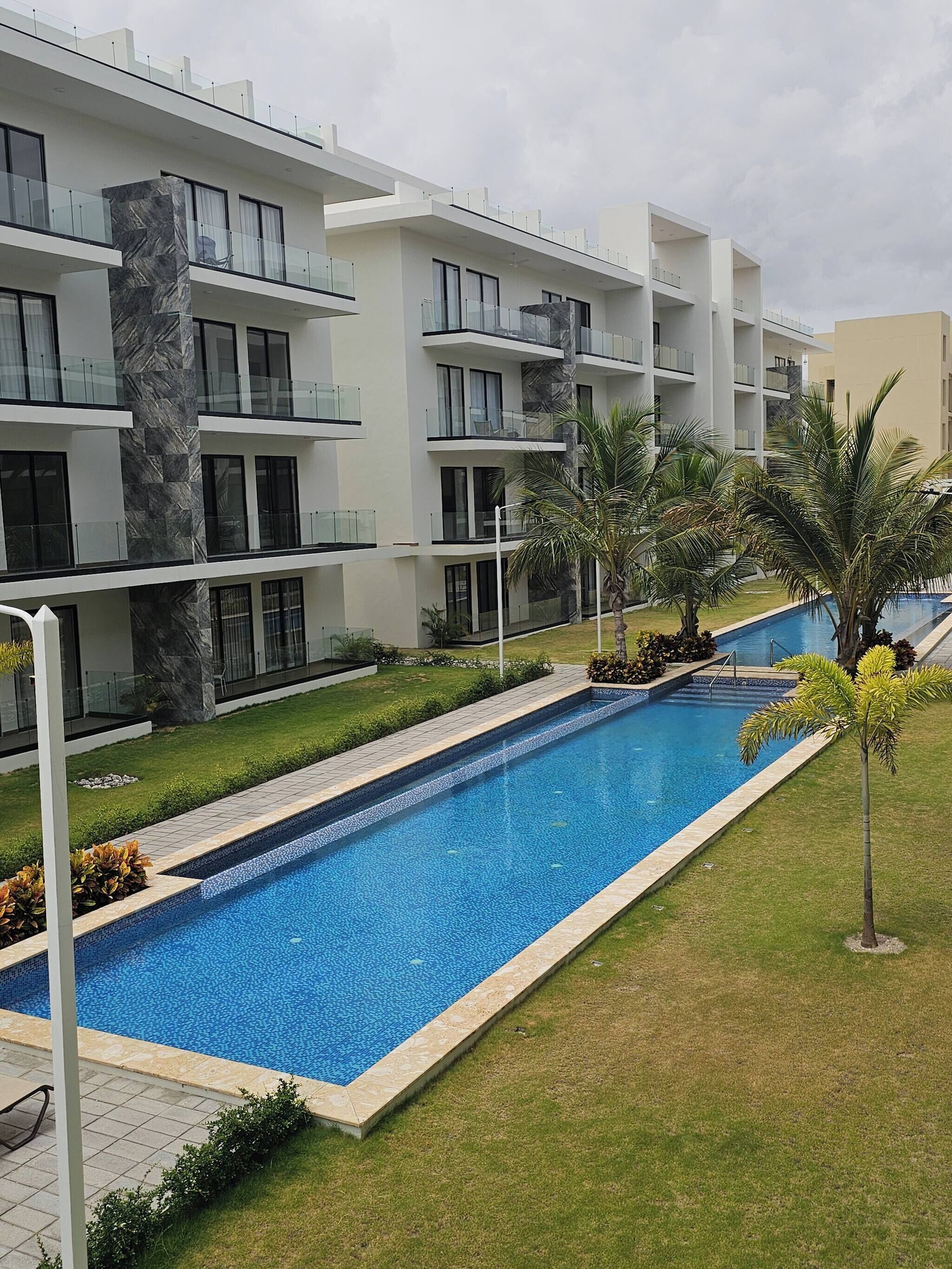 A modern hotel with a swimming pool, multiple balconies, and a well-maintained lawn.