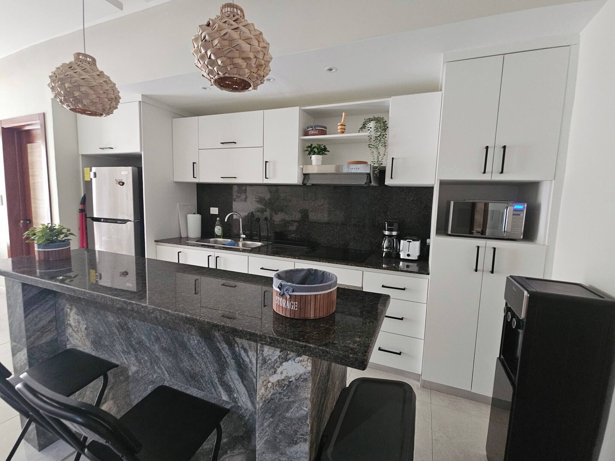 Una cocina moderna con armarios blancos, encimera negra y dos lámparas colgantes.