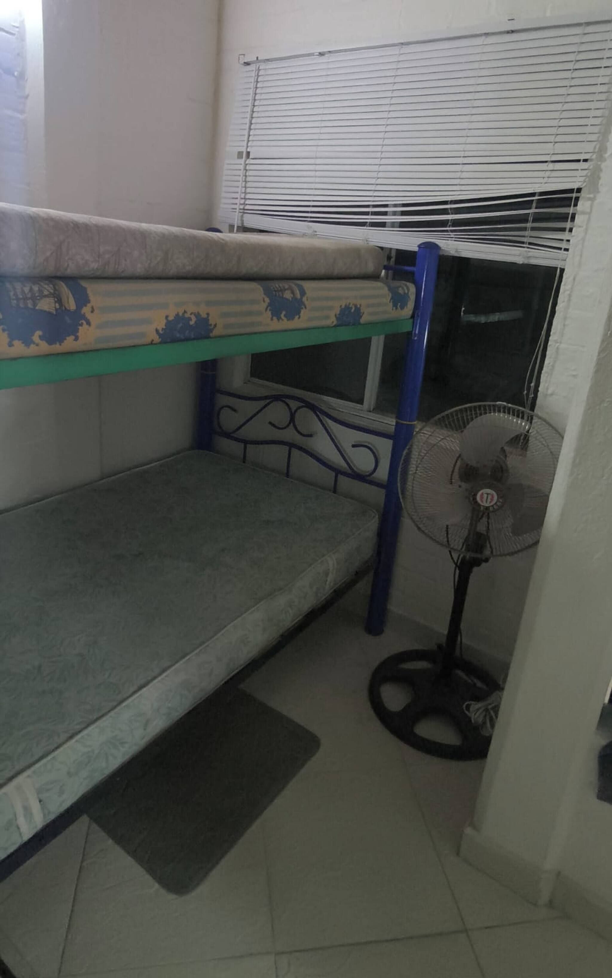 Una cama litera con colchón y ventilador en una habitación con suelo de baldosas.