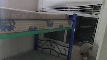 Una cama litera con colchón y ventilador en una habitación con suelo de baldosas.