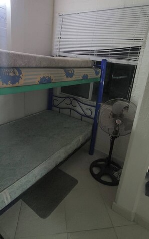 A bunk bed with a mattress and a fan in a room with a tiled floor.