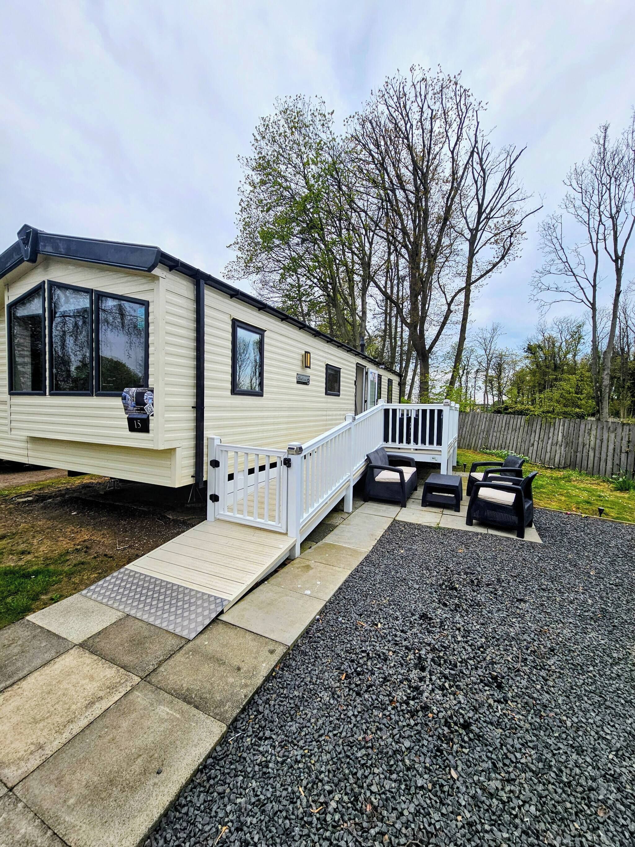 Une maison mobile dotée d’une terrasse, d’un espace salon extérieur et d’une allée en gravier.