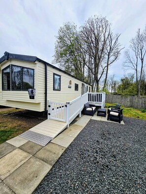 A mobile home with a deck, outdoor seating, and a gravel driveway. - Haggerston Castle Caravan Hire West Lawn MD (Haggerston)