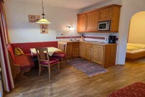 Uma cozinha compacta com armários de madeira, micro-ondas e um espaço de refeições com sofá vermelho e mesa.