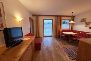 Um quarto acolhedor com uma escrivaninha de madeira, televisão, mesa de jantar com cadeiras e uma janela com cortinas.