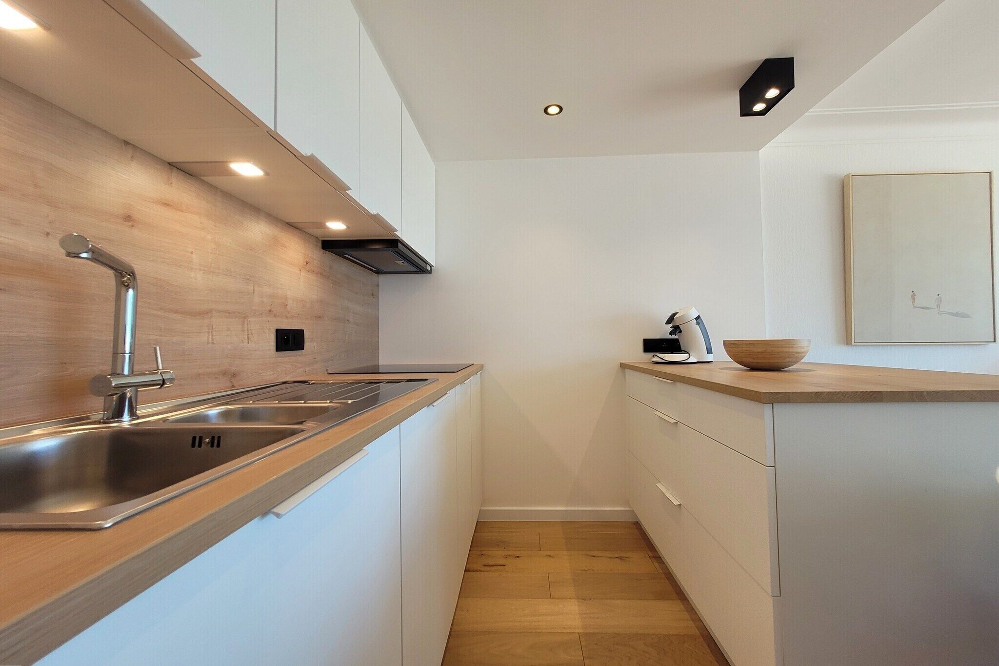 Une cuisine moderne dotée d’un évier en acier inoxydable, d’un plan de travail en bois et de meubles blancs.