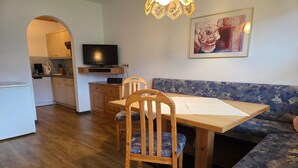 Cocina compacta con televisor, armarios de madera y un comedor con mesa y sillas.