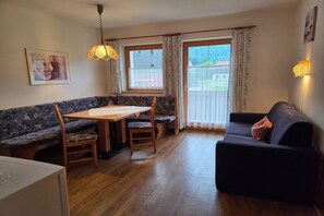 A dining area with a table and chairs, a sofa, and a window with curtains. - Holiday apartment near Lake Achensee (Achenkirch)