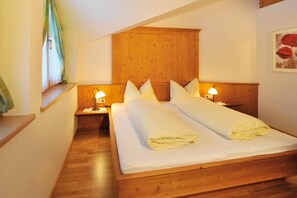 A double bed with wooden headboard and nightstands, a window with curtains, and a painting on the wall.
