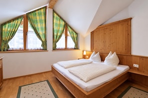 A bedroom with a wooden bed, two windows with plaid curtains, a nightstand with a lamp, and a wooden headboard. - Alpine holiday apartment near a lake (Achenkirch)