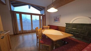 Et spiseområde med et træbord, stole og bænke. Der er et vindue med gardiner, en vægmonteret lampe og et kunstværk på væggen.