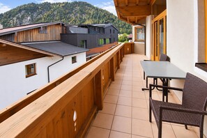 A balcony with a wooden railing, a table, and chairs, overlooking a mountain and neighboring buildings. - Alpine holiday apartment near a lake (Achenkirch)