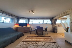 Habitación compacta con cama, escritorio con computadora, mesa de comedor con sillas y kitchenette.