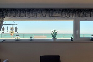 Una habitación con un amplio ventanal con vistas a una playa, una decoración de pez colgante y una planta en maceta en el alféizar.