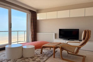 Ein modernes Schlafzimmer mit großem Fenster, Fernseher, Bett, Sessel und kleinem Tisch.
