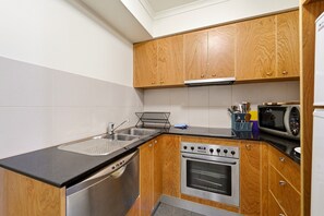 A compact kitchen with wooden cabinets, a stainless steel sink, a microwave, and an oven. - City-Edge 1-Bed Apartment with Pool Access (City)