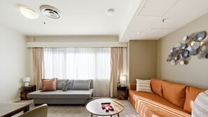 Quarto de hotel com sofá, mesa pequena, cama e um objeto decorativo na parede.
