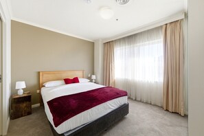 Ein Hotelzimmer mit einem Bett, einem Nachttisch mit Lampe und einem Fenster mit Vorhängen.