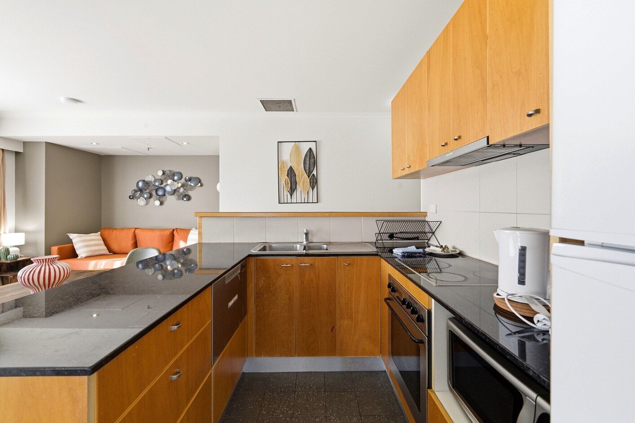 A compact kitchen with wooden cabinets, a black countertop, and a built-in oven.