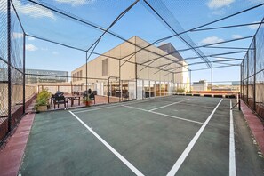 Ein Tennisplatz mit Netz, umgeben von einem Zaun, und ein Gebäude im Hintergrund.