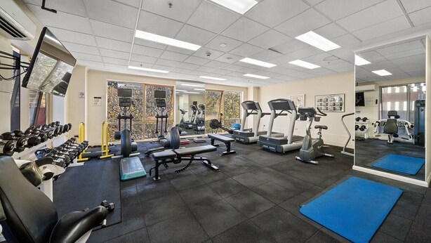 Uma academia com diversos equipamentos de exercício, incluindo esteiras, aparelhos de musculação e pesos livres.
