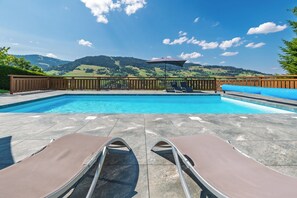 Ein Swimmingpool mit zwei Liegestühlen und einem Holzzaun, eingebettet in eine gebirgige Landschaft.