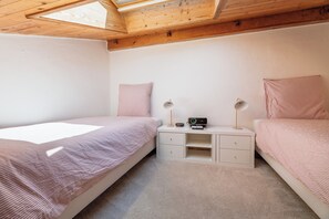 Ein Schlafzimmer mit zwei Einzelbetten, einem Nachttisch mit Radio und Lampe sowie einem Oberlicht.