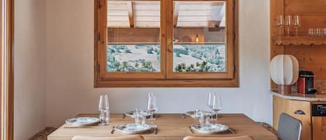 Une table de salle à manger en bois, donnant sur un paysage enneigé par la fenêtre.