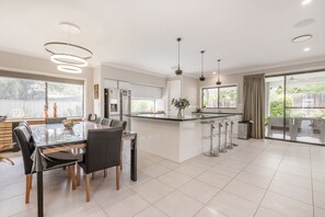 A modern kitchen with a central island, bar stools, and a dining area with a table and chairs. - Charming 4-Bed Getaway with Pool & Garden Oasis (Curtin)