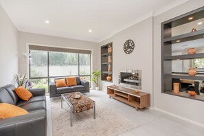 A modern living room with a sofa, coffee table, TV, and built-in shelves. - Charming 4-Bed Getaway with Pool & Garden Oasis (Curtin)