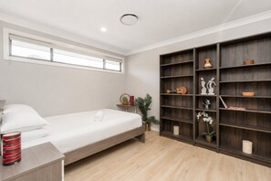 A modern bedroom with a single bed, a nightstand, a bookshelf, and a window. - Charming 4-Bed Getaway with Pool & Garden Oasis (Curtin)
