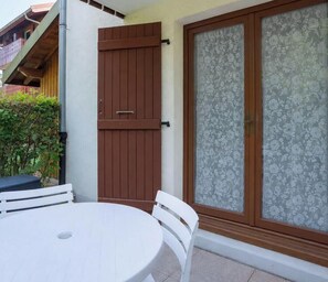 Eine Terrasse mit einem runden Tisch und weißen Stühlen, einer Holztür sowie einer Glastür mit floralem Dekor.