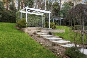 A garden with a white pergola, stone steps, and a metal table and chair set.