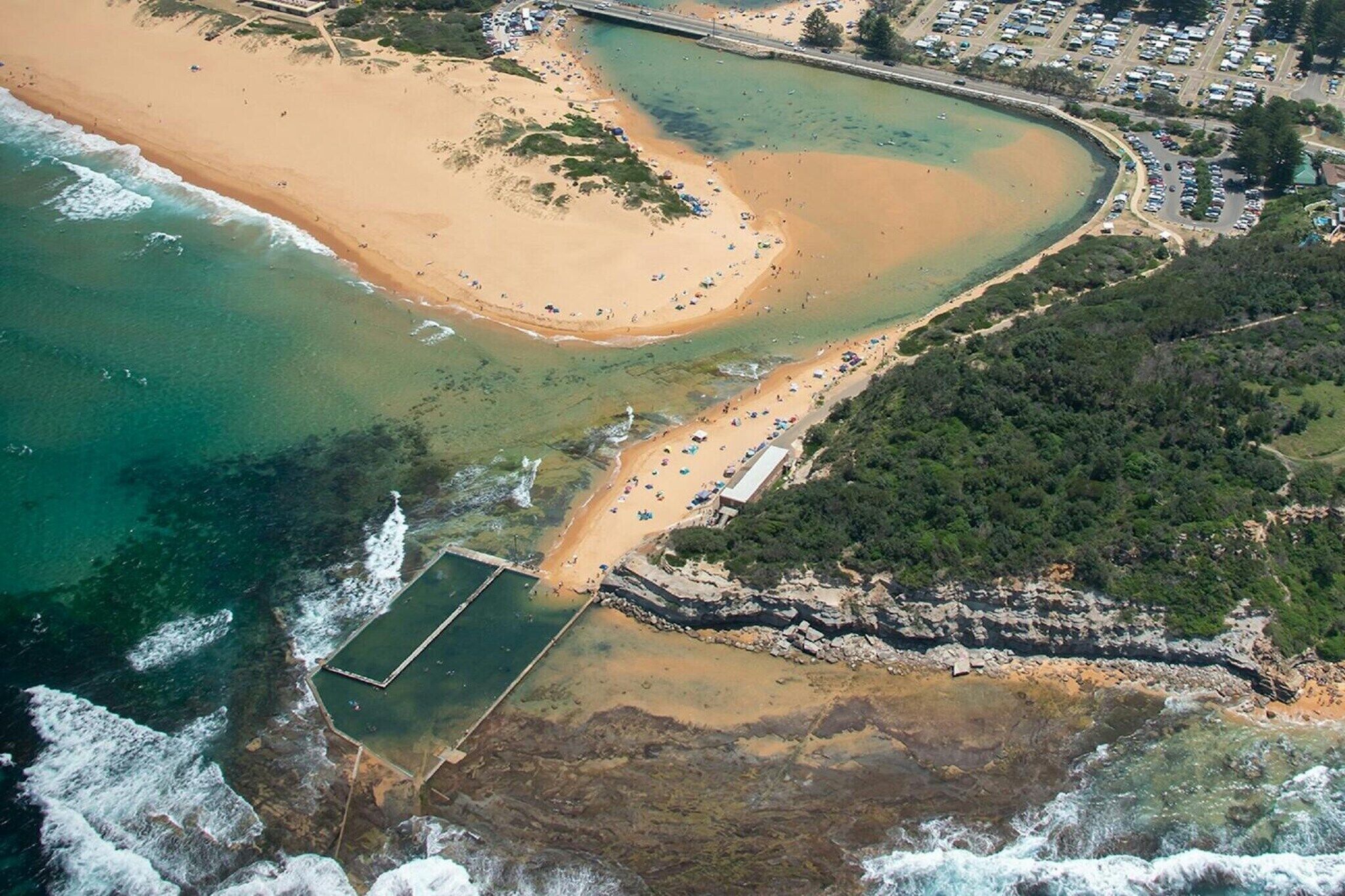 Vista aérea de uma área costeira com praia, marina e um litoral rochoso.