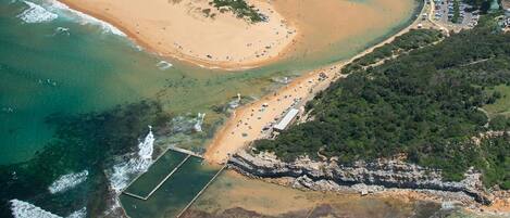 Vista aérea de una zona costera con playa, puerto deportivo y costa rocosa.