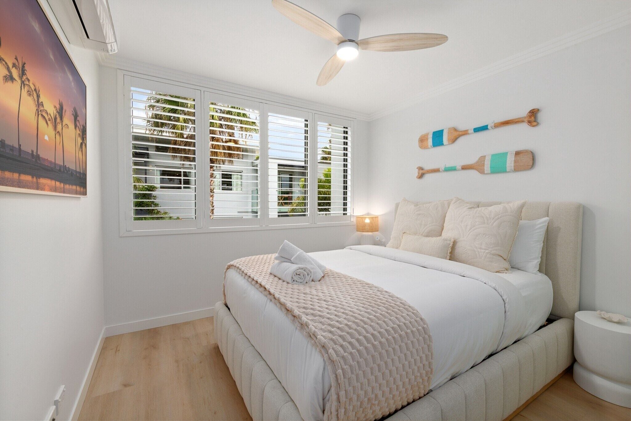 A bedroom with a bed, a ceiling fan, a window with blinds, and a wall-mounted lamp.