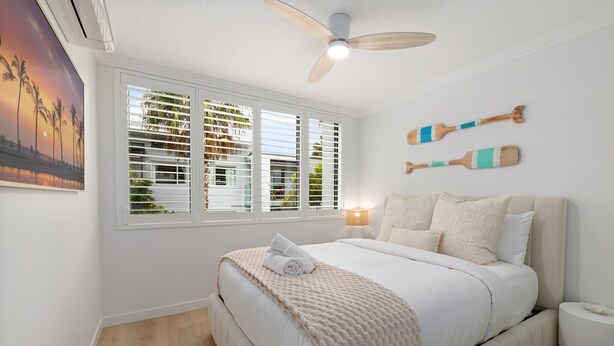 A bedroom with a bed, a ceiling fan, a window with blinds, and a wall-mounted lamp. - Beach & Lake Narrabeen Apartment with Outdoor BBQ (Narrabeen)