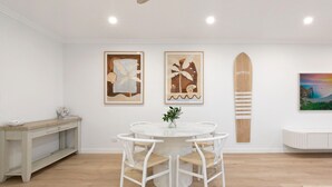 A dining area with a round table and chairs, a bench, and artwork on the walls. - Beach & Lake Narrabeen Apartment with Outdoor BBQ (Narrabeen)