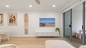 A modern living room with a white sofa, a white coffee table, a white cabinet, and a beach-themed artwork. - Beach & Lake Narrabeen Apartment with Outdoor BBQ (Narrabeen)