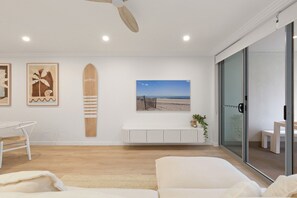 Ein modernes Wohnzimmer mit einem weißen Sofa, einem weißen Couchtisch, einer weißen Kommode und einem Kunstwerk zum Thema Strand.
